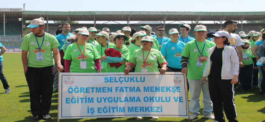 DEKALB'ın desteklediği 2. Özel Sporcular Atletizm Oyunları'na katılan öğrenci grubu okulunun pankartı önünde poz veriyor